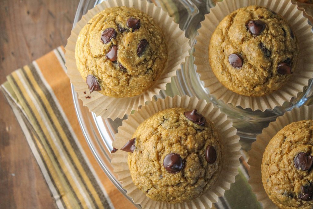 over head shot of pumpkin oat hemp muffins studded with chocolate chips on a clear glass cake platter in natural baking paper cups