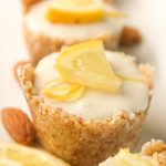 a row of lemon cheesecake tartlets in a raw nut crust with a garnish of fresh lemon slices on a white plate