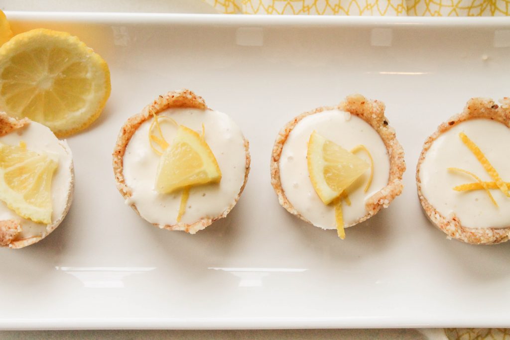 4 creamy lemon cheesecake tarts on a white plate with lemon slice garnish