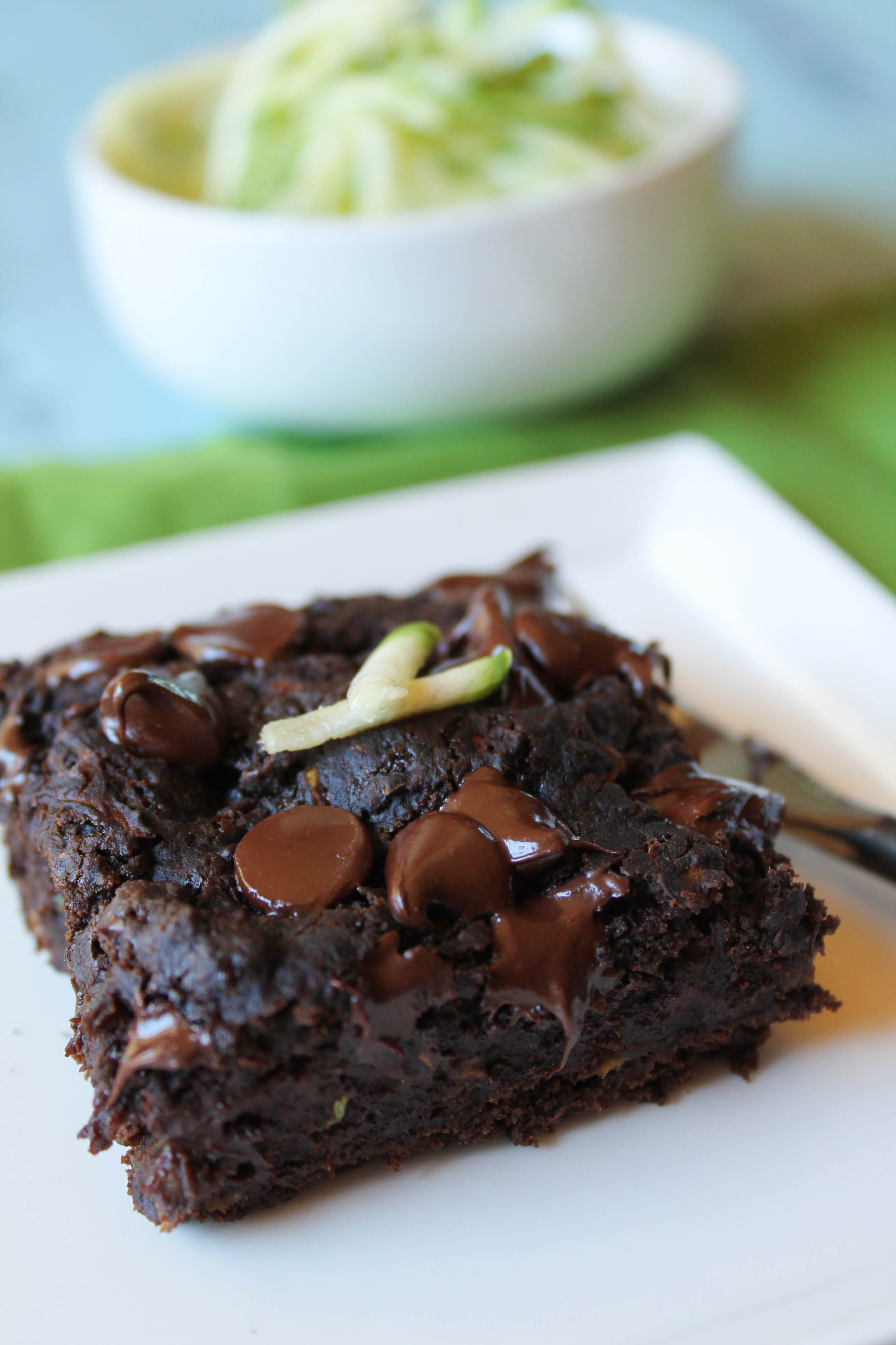 a square of moist chocolate zucchini cake topped with gooey chocolate chips and a few fresh zucchini shreds