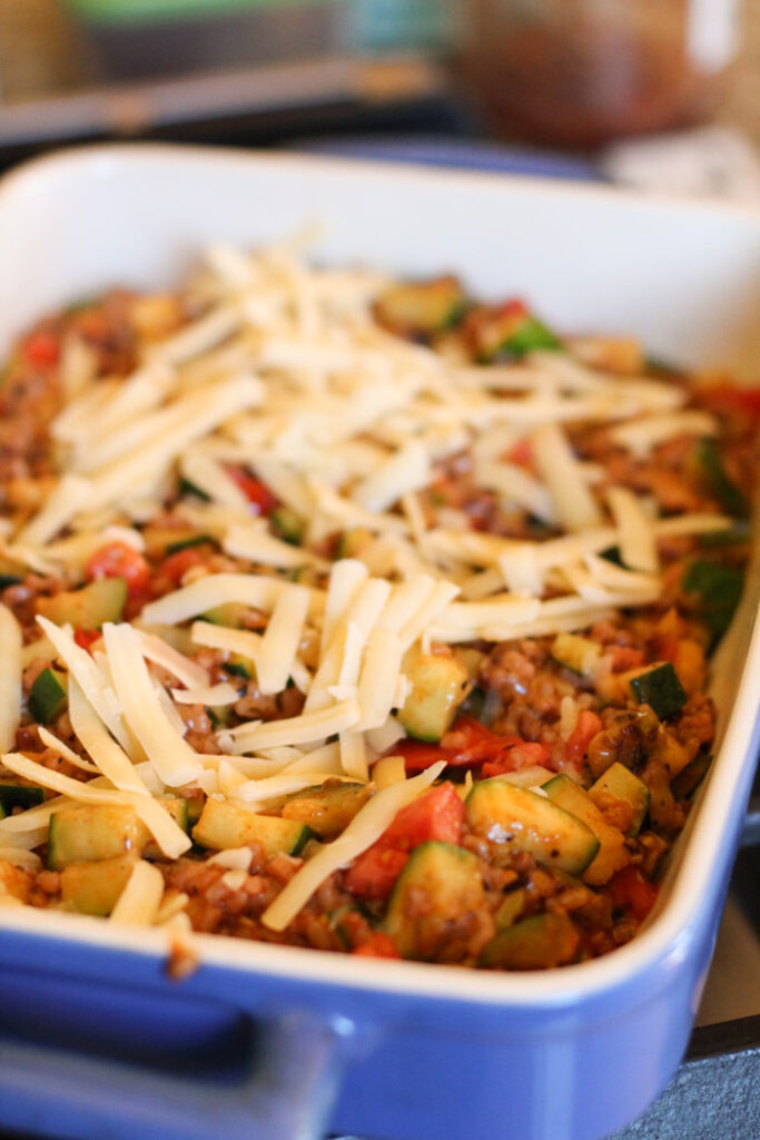 blue casserole pan with cheese topped zucchini casserole