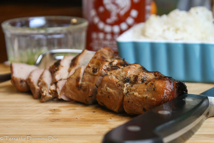 sliced pork tenderloin with rice and green on a bamboo cutting board