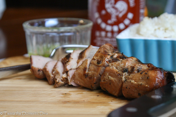 eye level image of a sliced marinated pork tenderloin with Sriracha and green onions on a wooden cutting board