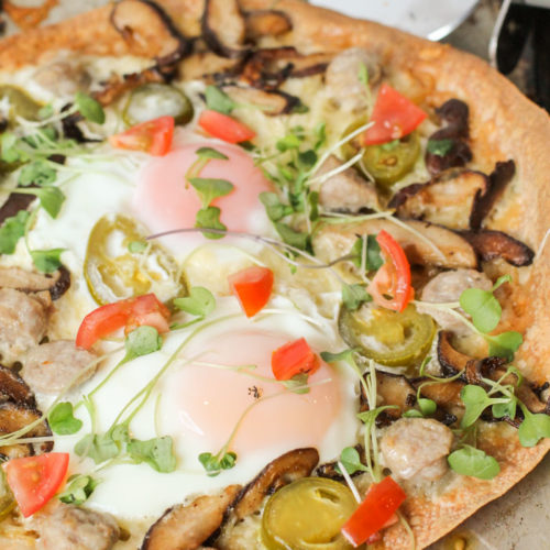 from the front view of a crispy brown rice tortilla topped with fresh veggies, molten eggs atop a worn cookie sheet