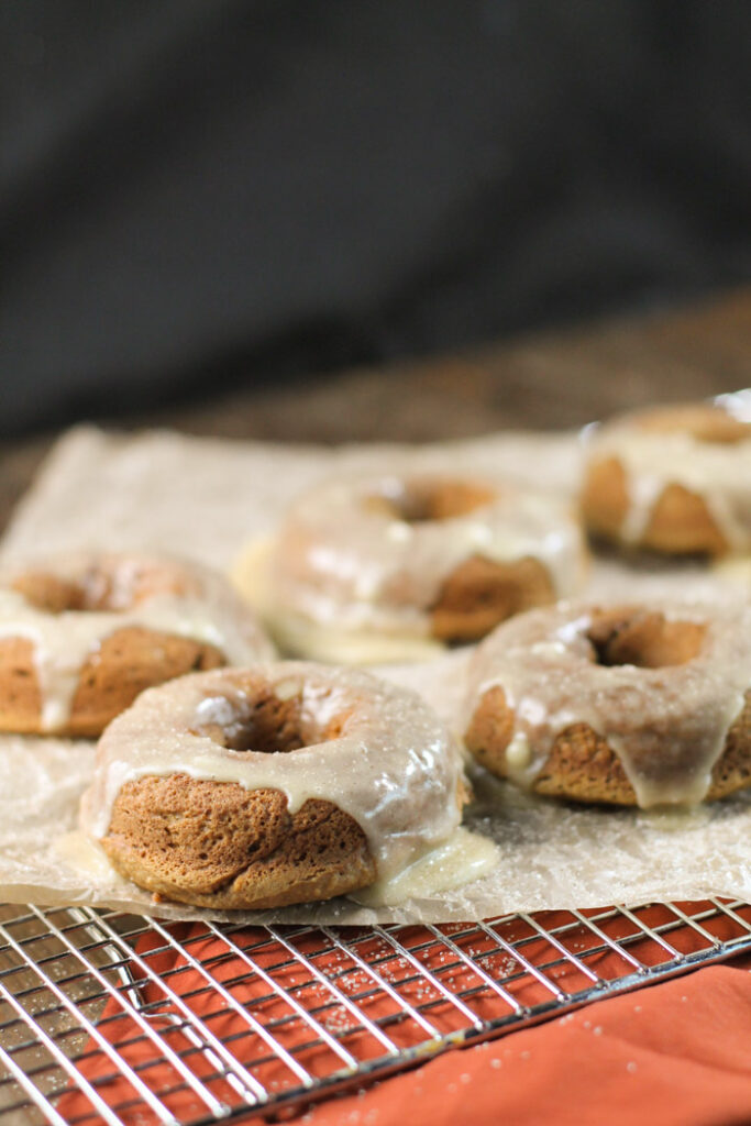 many frosted pumpkin donuts on a cooling rack