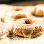 horizontal picture of glazed pumpkin donuts at eye level atop a piece of parchment paper
