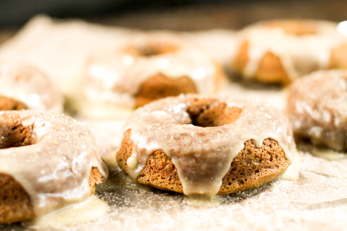 horizontal picture of glazed pumpkin donuts at eye level atop a piece of parchment paper