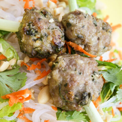 overhead view of three meatballs with cilantro, shredded carrots, chopped nuts, and lemongrass skewers