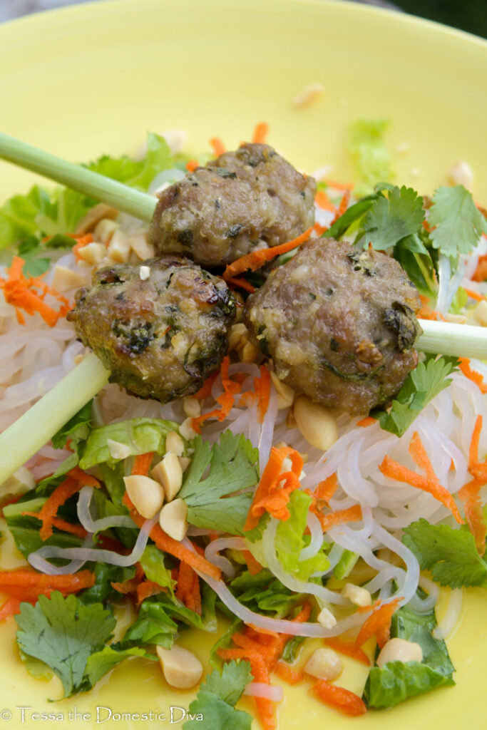 front view of three vietnamese pork meatballs with a lemongrass skewer atop noodles and veggies