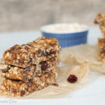 three stacked homemade granola bars on a parchment paper with cranberries.