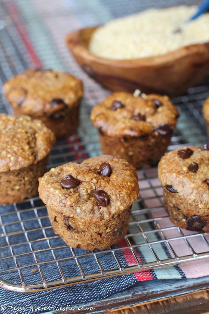 mini muffins with whole millet and chococlate chips on a coling rack with an olive wood bowl of millet grain in background