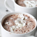 two white mugs filled with cocoa topped with whipped cream