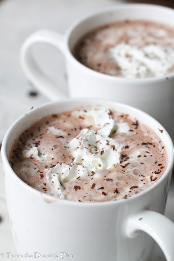two white mugs filled with cocoa topped with whipped cream