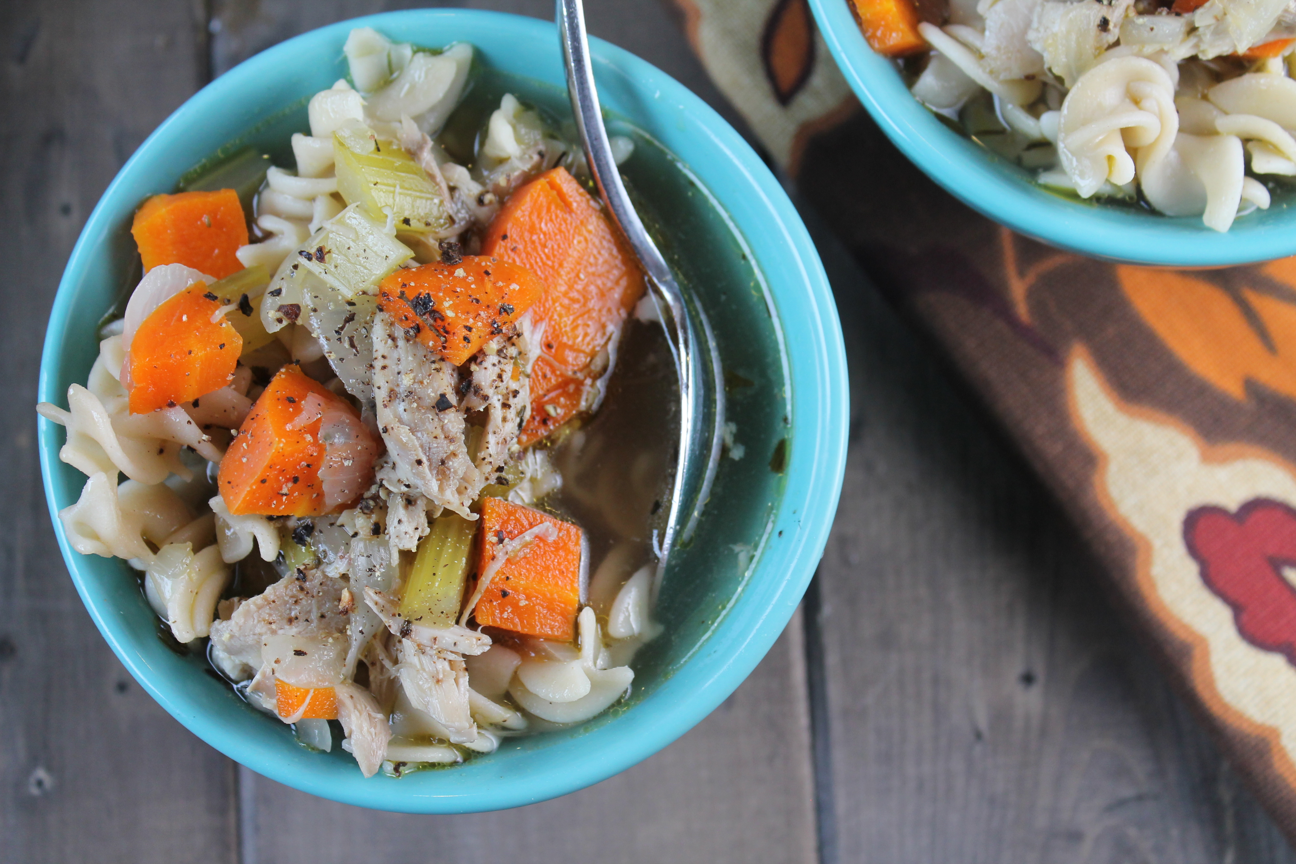 birdseye view of two aqua bowl filled with noodles, broth, carrot chunks, and celery