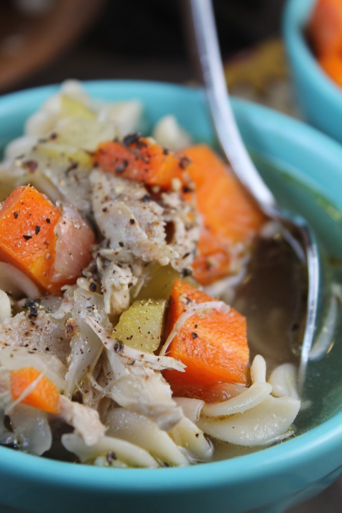 close up of turkey, celery, and carrot chunks in a chicken soup in a turquoise bowl