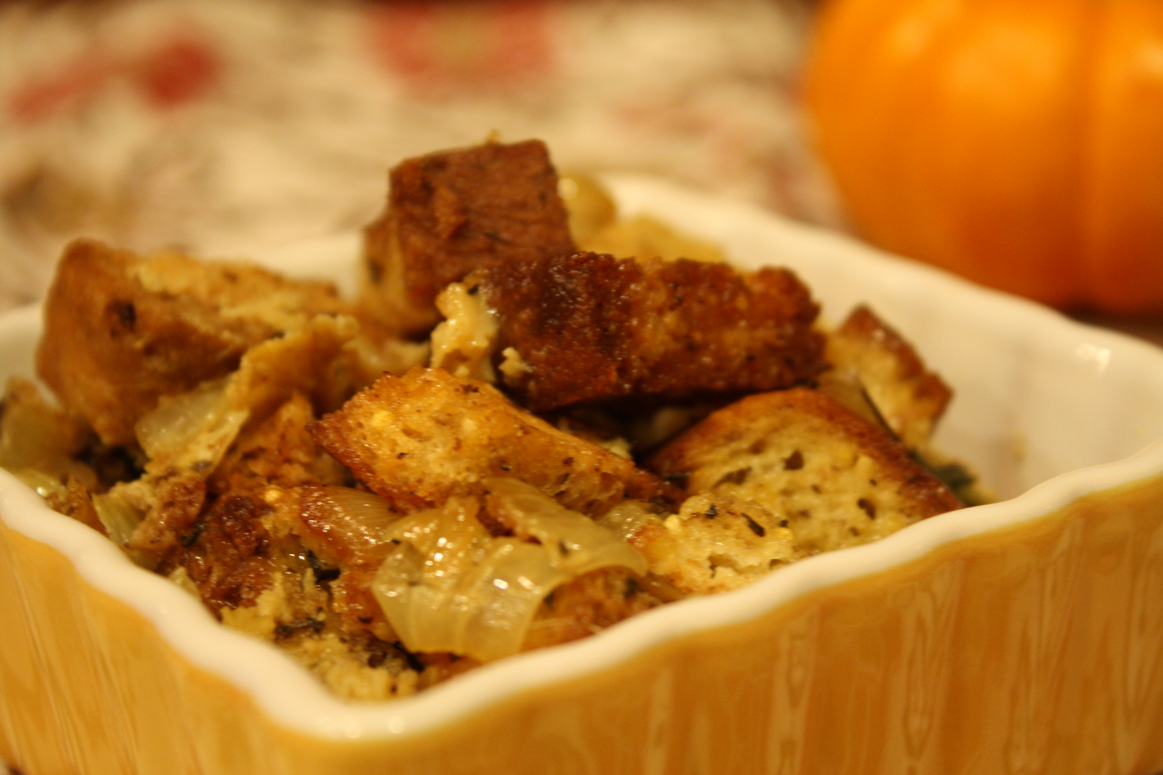 a paleo yellow white ceramic baking dish filled with toasted bread cubes in a broth, celery, and and onion stock