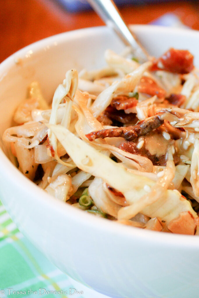 eye level close up up of a white bowl filled with cabbage slaw with bacon in a vinaigrette