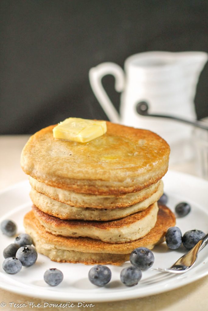 a stack of diner like pancakes with a pat of golden butter and fresh blueberries on a white plate with black background