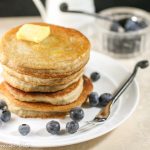 a stack of fresh golden pancakes with a pat of butter and fresh blueberries on a white plate