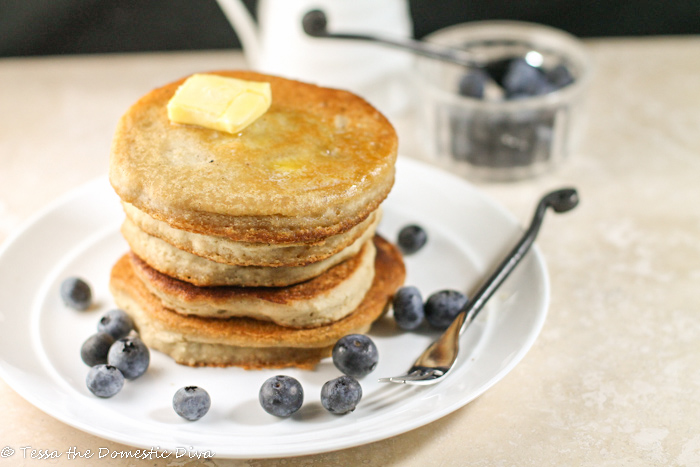 a stack of fresh golden pancakes with a pat of butter and fresh blueberries on a white plate