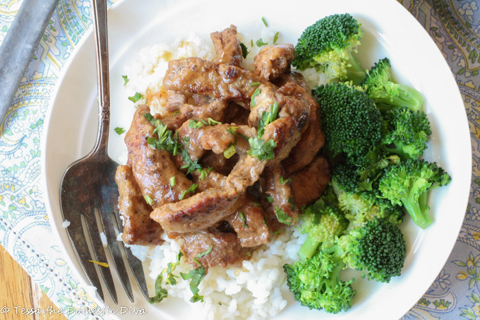 birdseye view of a white bowl filled with rice, broccoli, and tnder steak strips in gravy with a chopped parsley garnish