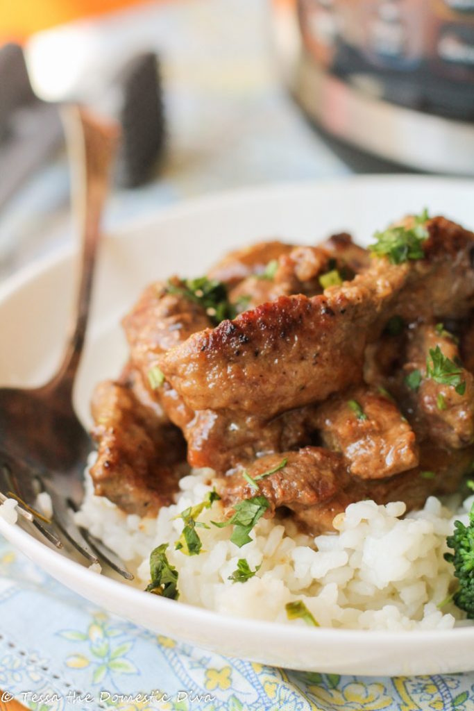 strips of tender steak coated in a savory gravy on top of a bed of white rice with a side of broccoli in a white bowl with an Instant Pot in the background