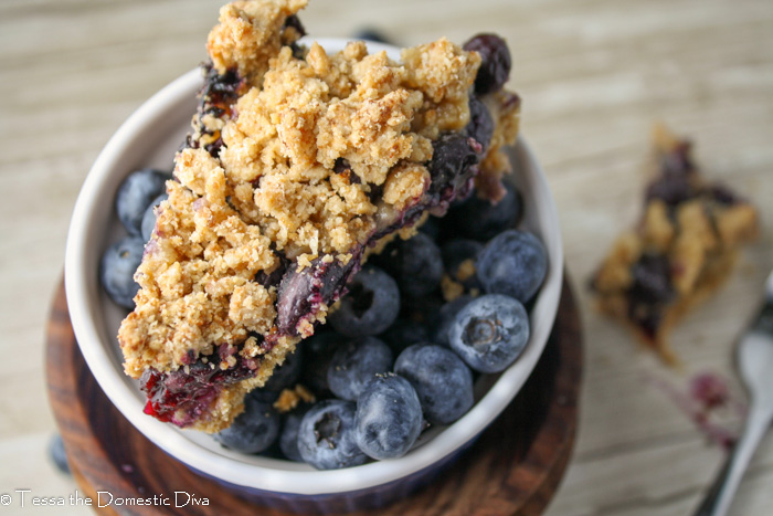 birds eye view of a piece of blueberry crumble bars atop a bowl of fresh blueberries
