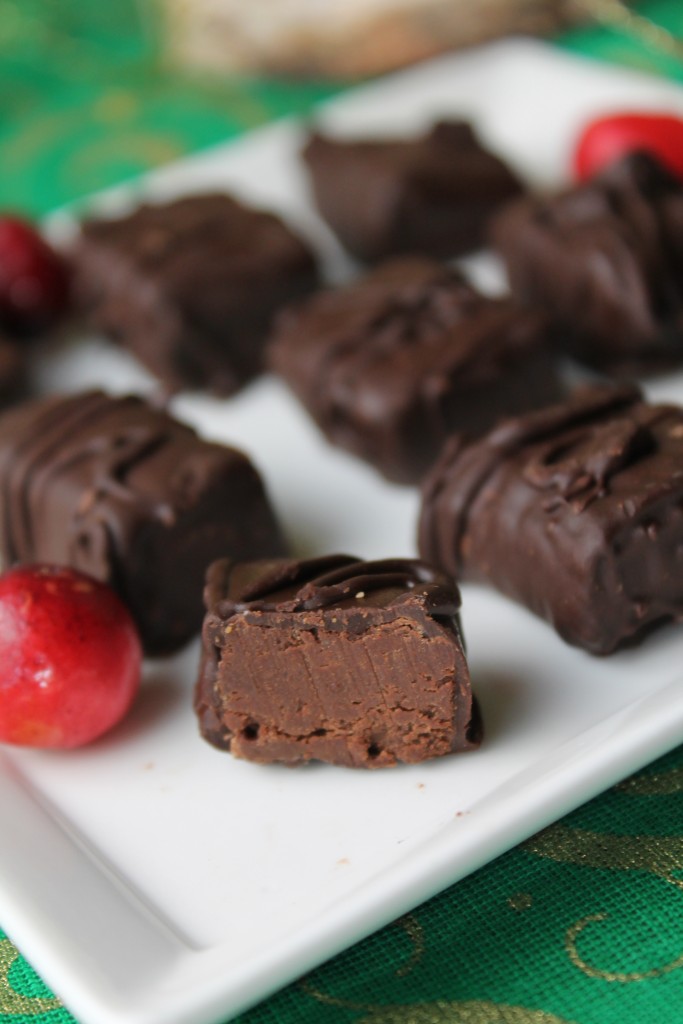 verical image of dipped chocolate mint truffles with one sliced for view of soft minty center on a white plate with fresh cranberries and a dark green tablescloth