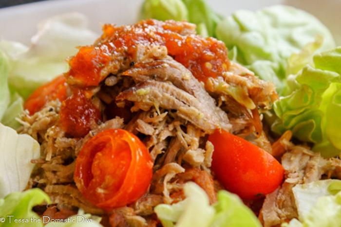 close up eye level view of tender shreds of pulled pork shoulder in a green chile sauce with cherry tomato halves atop butter lettuce