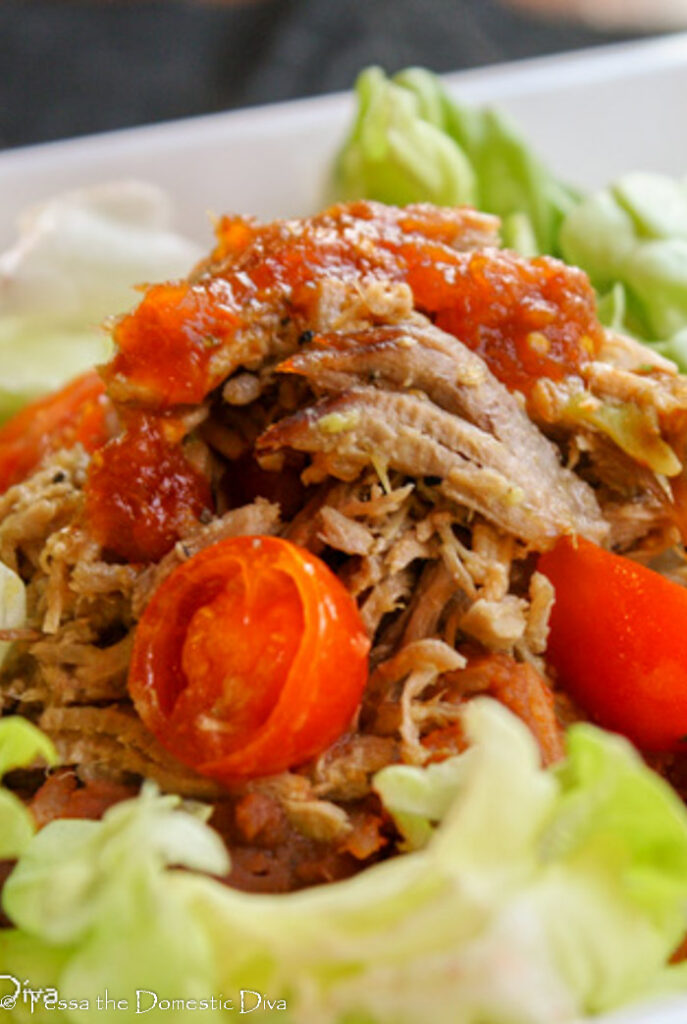 pulled pork for tacos close up on a bed of lettuce with halved cherry tomatoes