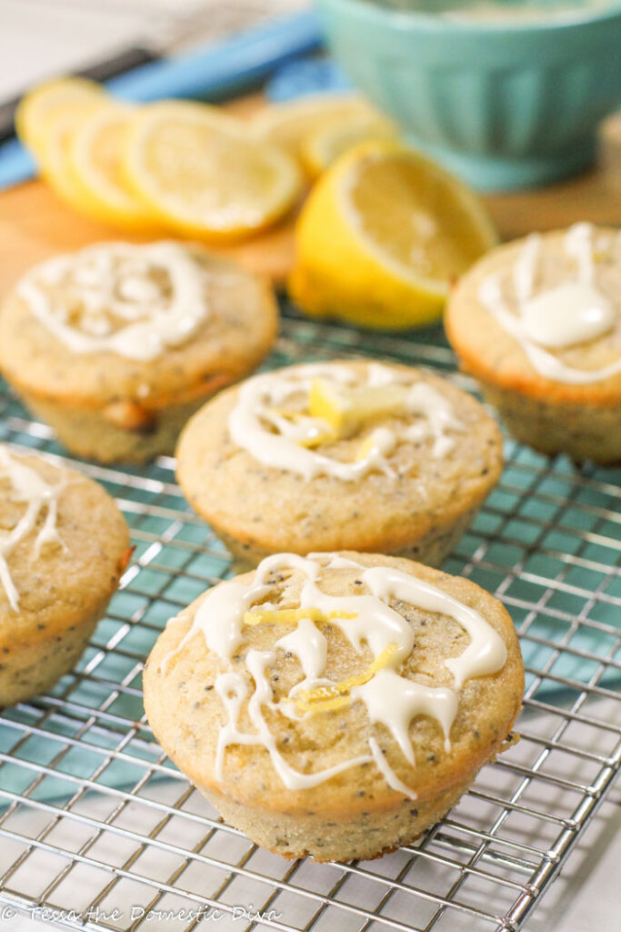 lemon glazed lemon poppyseed muffins arranged on a cooling rack with a turquiose linen and sliced fresh lemon