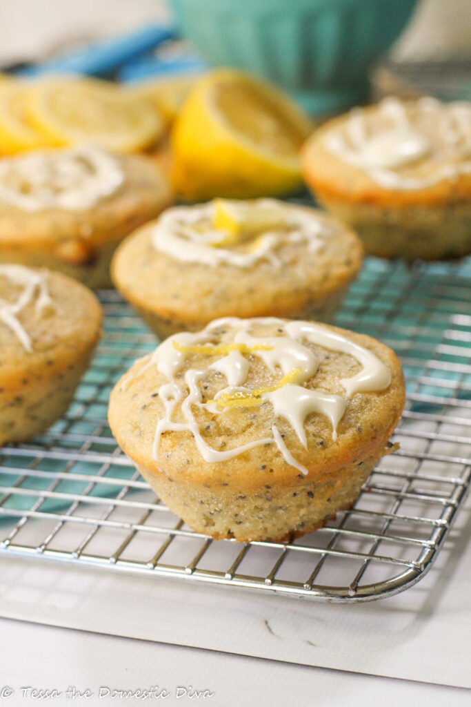 lemon glazed poppy seed muffins on a steel cooling rack with a lemon zest garnish