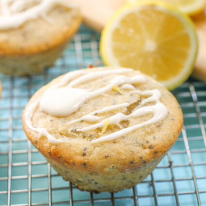 swirled lemon frosting atop a lemon poppy seed muffin with a sliced lemon half and pale turquoise cloth