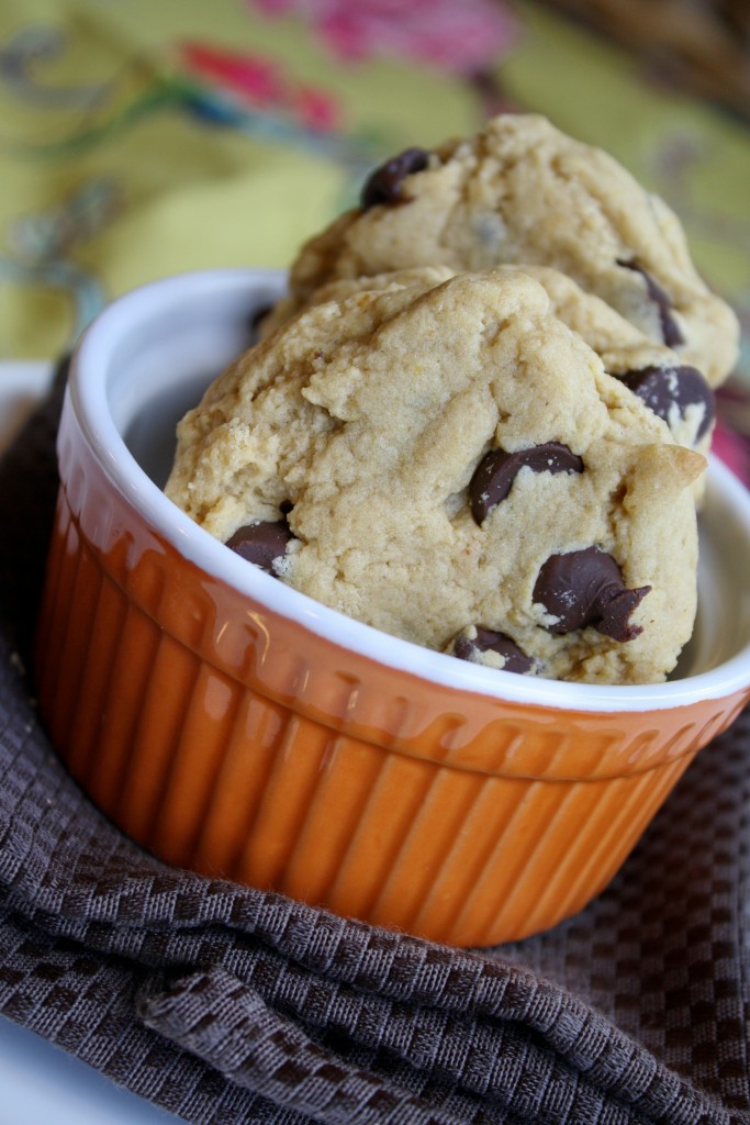 vertical image of two chocolate chip studded cookies standing on end in a pumpkin orange ramekin