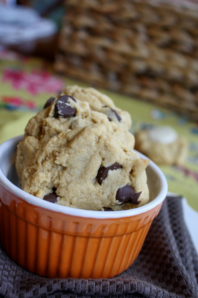 two golden cookies with chocolate chips in a dark orange ramekin with a natural woven basket in the background