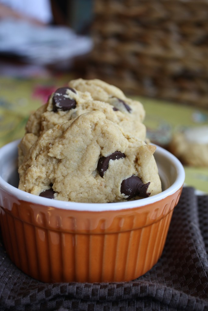 orange ramekin filled with several orange hued chocolate chip studded cookies on a brown linen