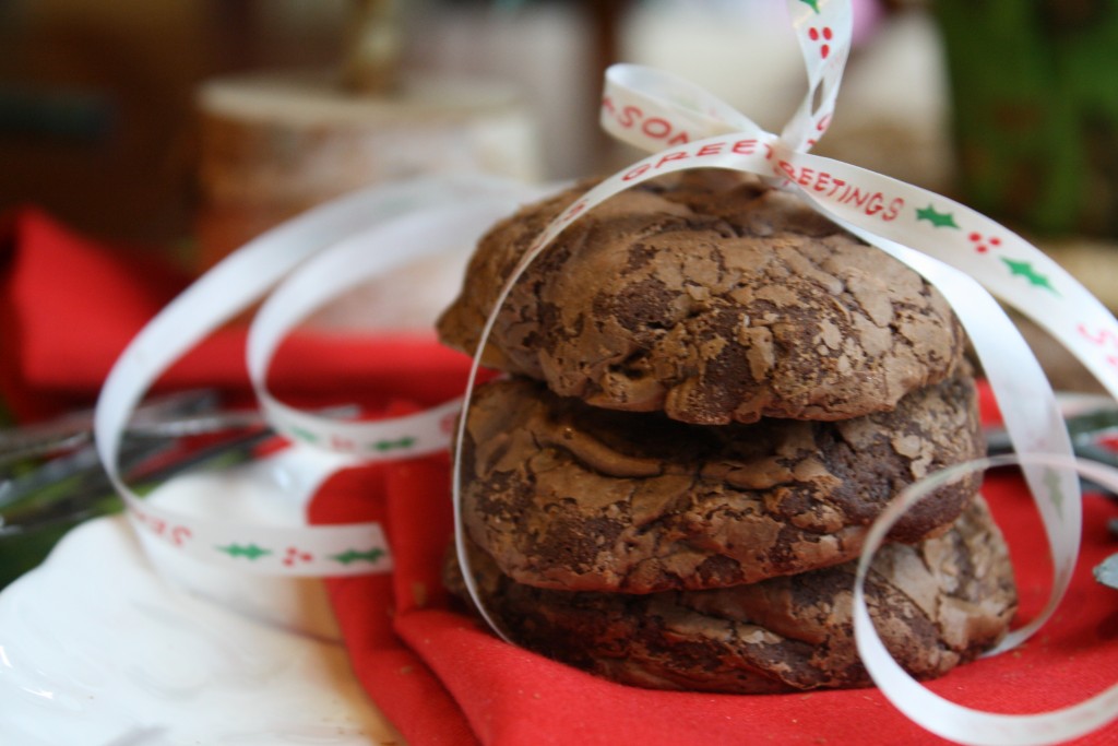 horizontal image of three stacked chocolate cookies wrapped with a seasons greetings Christmas ribbon on a red linen from eye level and close up
