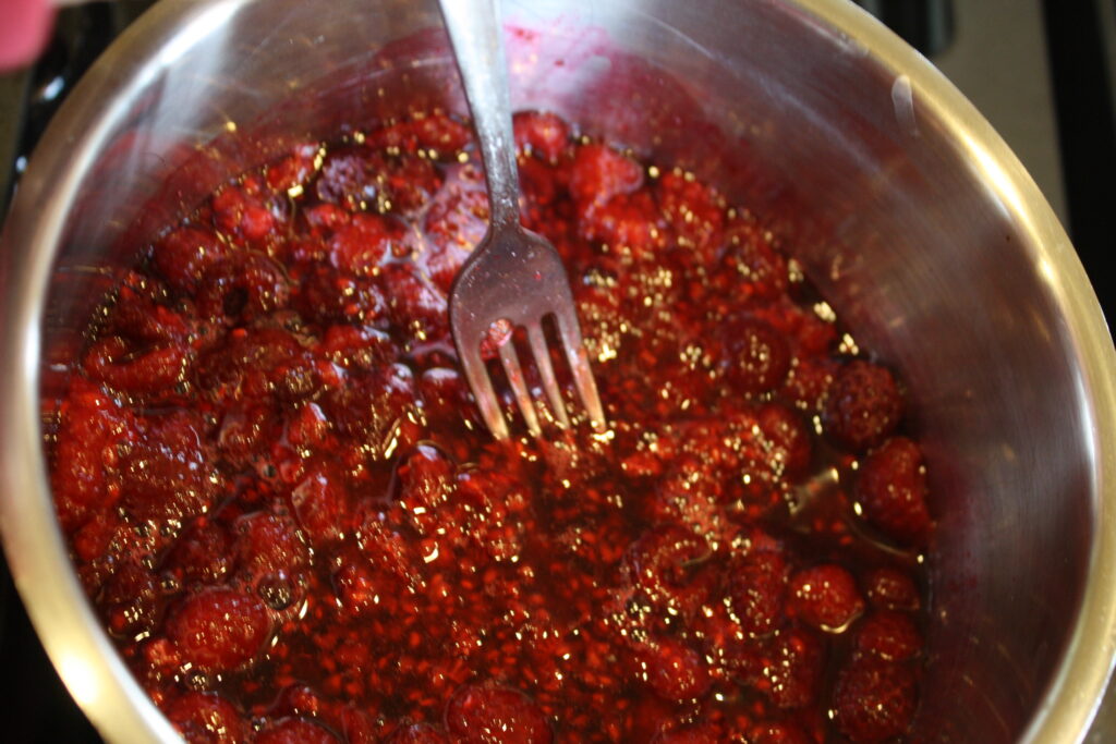 cooked mashed raspberries in saucepan with a fork stirring