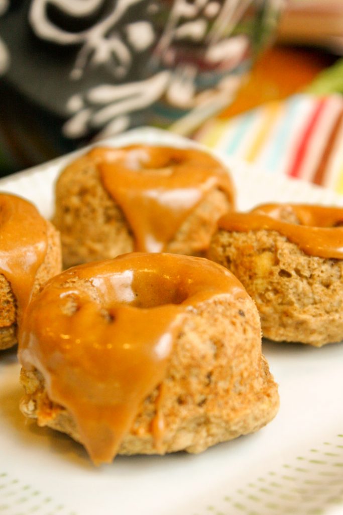 4 caramel glazed mini donuts arranged on a white plate with a colorful striped cloth