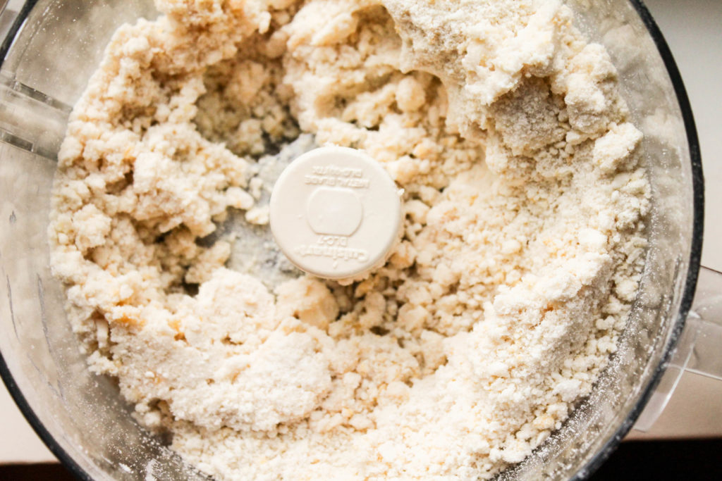 overhead view of a crumbled biscuit dough in a food processor bowl.