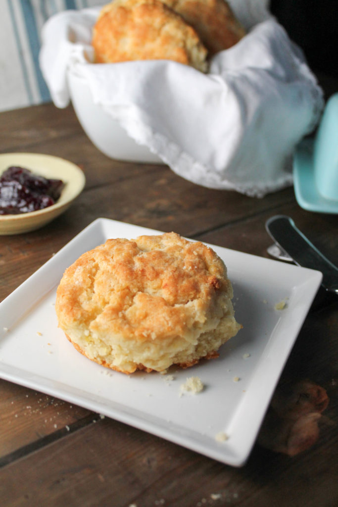 A single golden biscuit on white plate with jelly and fresh butter.