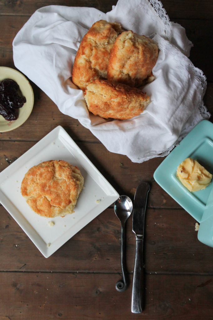 an arrange of golden biscuits on a dark wood surface with butter and jelly.