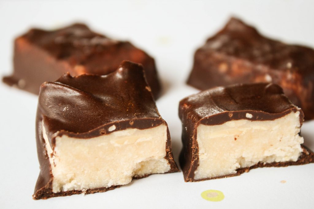 eye level close up of copycat paleo coconut secret bars sliced in half on a pale blue surface