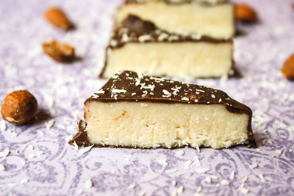 homemade triangle shaped mounds bars coated in a thin chocolate layer on a purple floral fabric surrounded by whole almonds