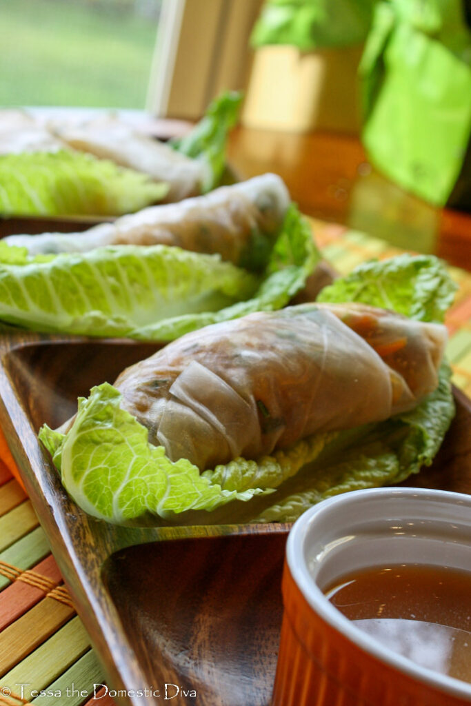 a dark wooden tray with fresh summer rolls on lettuce leaves.