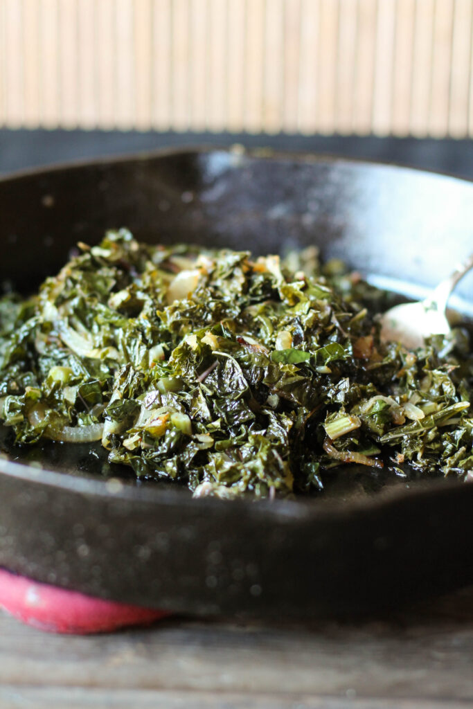 a black cast iron pan filled with chopped sauteed kale with caramelized onions