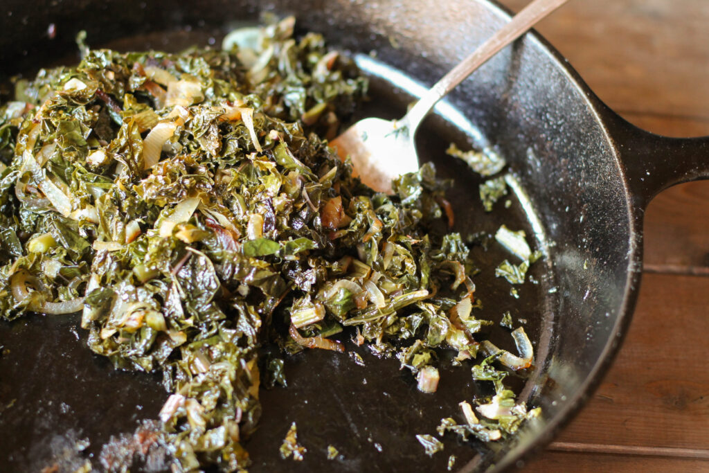 a silver serving fork in a black cast iron pan filled with sauteed kale and onions