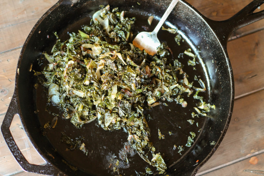 chopped dinosaur kale and sliced caramelized onions in a cast iron pan on a wooden a pallet from overhead