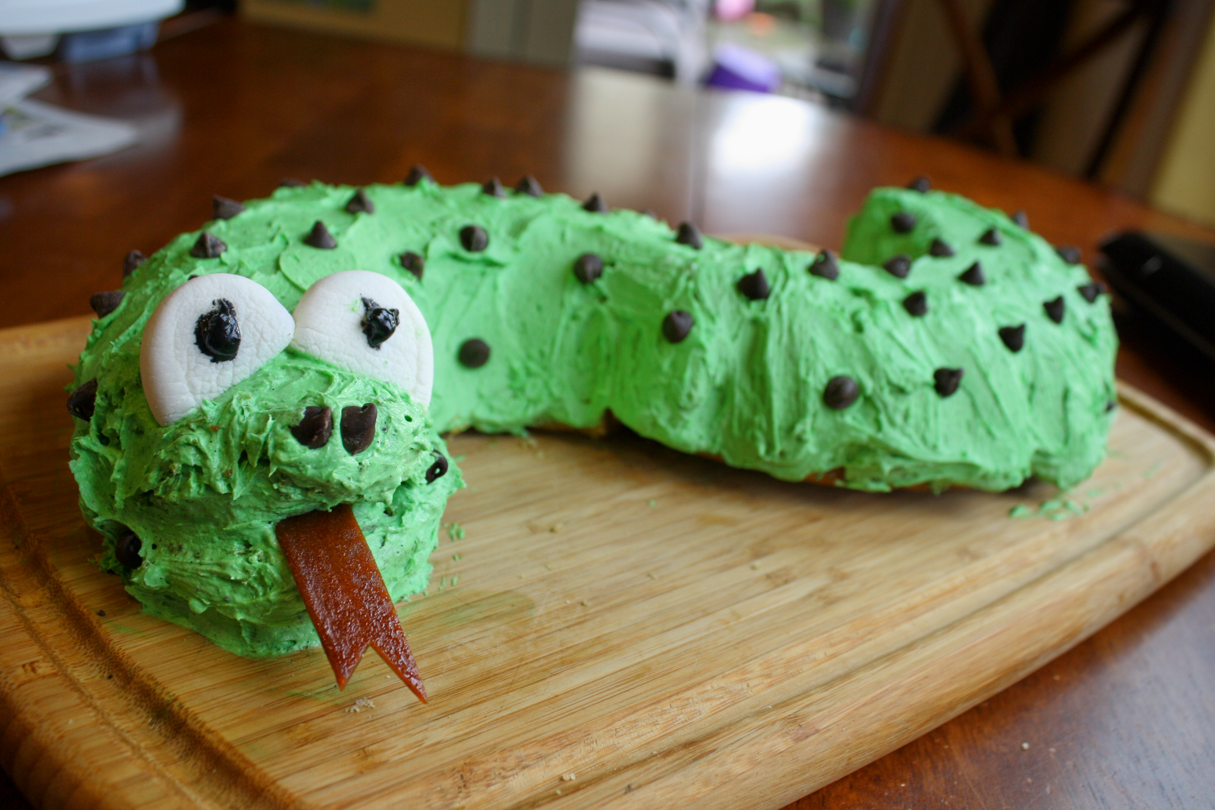 a snake shaped vanilla cake with green frosting on a wooden cutting board
