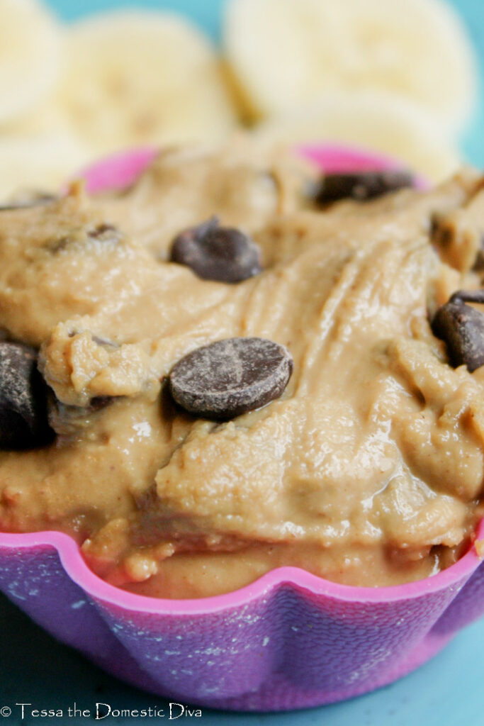 close up of a pink muffin liner filled with a peanut butter chocolate dip with fresh banana slices